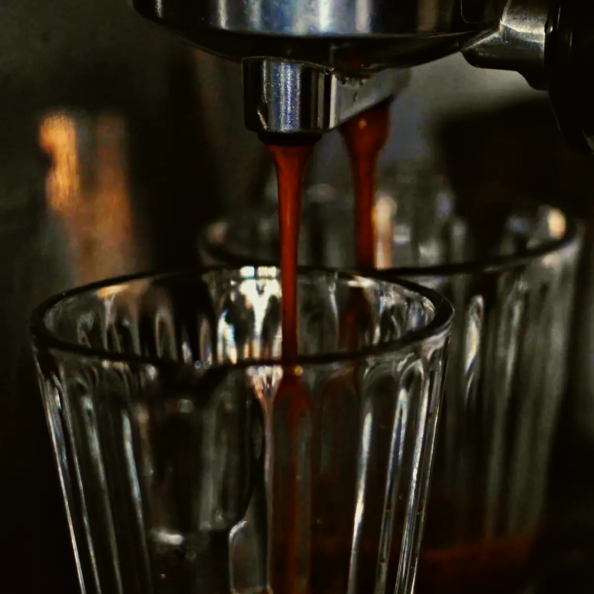 Twee dunne stralen espresso lopen uit de machine in een glas
